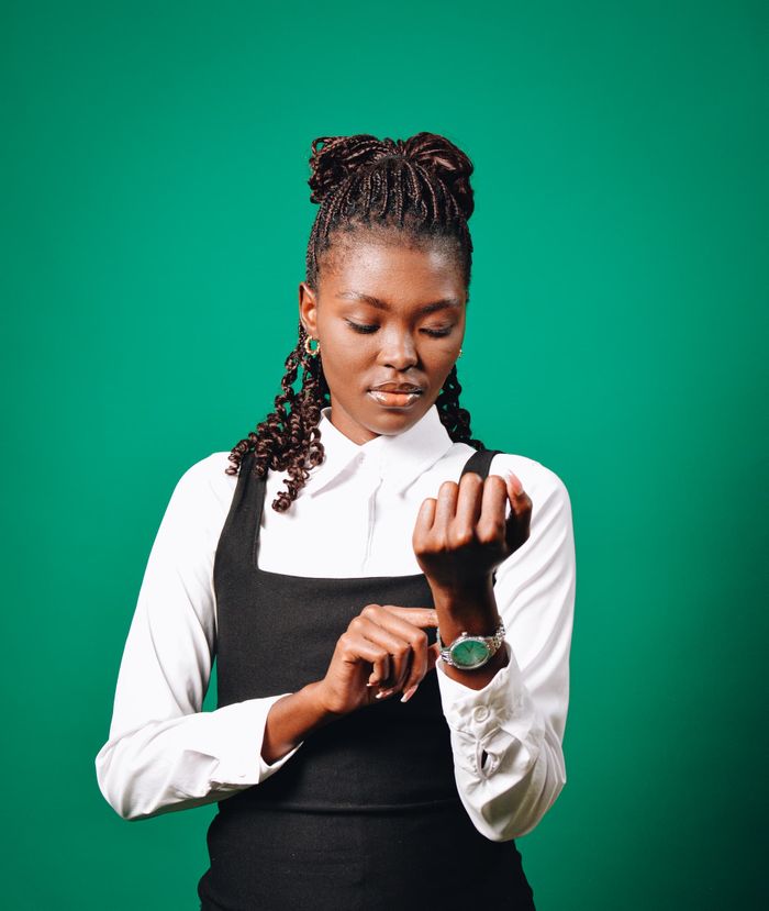 Professional woman in formal attire checks her watch against a green backdrop.