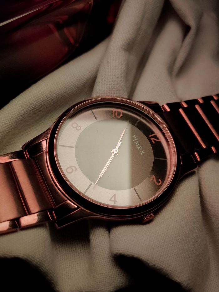 Rose gold wristwatch on white fabric with soft lighting and rich tones.